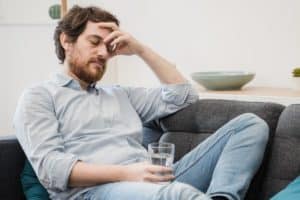 a man holds his head while gripping a glass of water