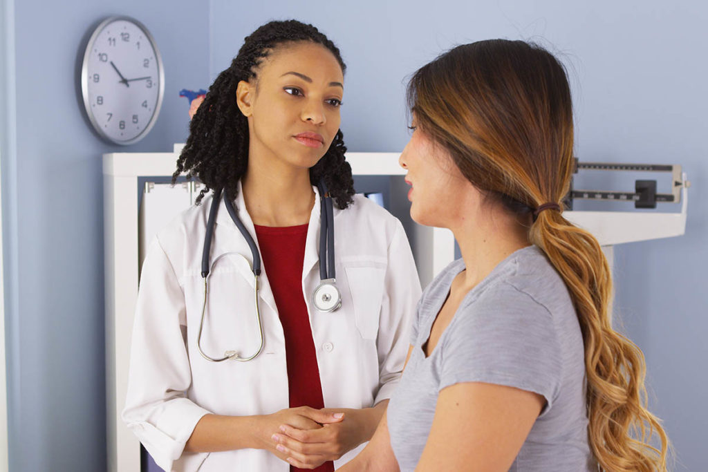 a doctor stands and explains apartial hospitalization program option to a sitting patient