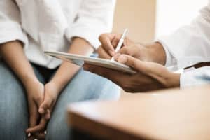 a pair o0f hands takes note while another pair sits in a lap during an alcoholism treatment program