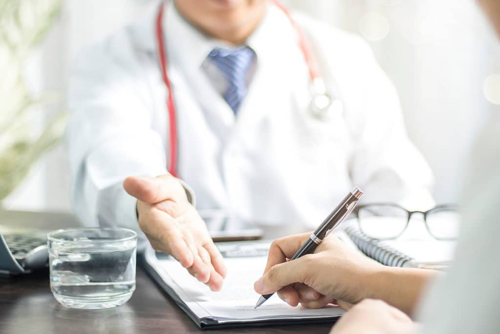 a doctor sits at a desk in front of a patient and provides a partial hospitalization program definition