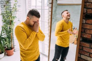 a sad person looks happy in a mirror struggling with Bipolar symptoms