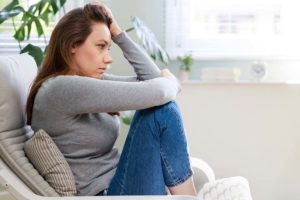 a person sits on a couch holding their head struggling with Mental health and substance abuse